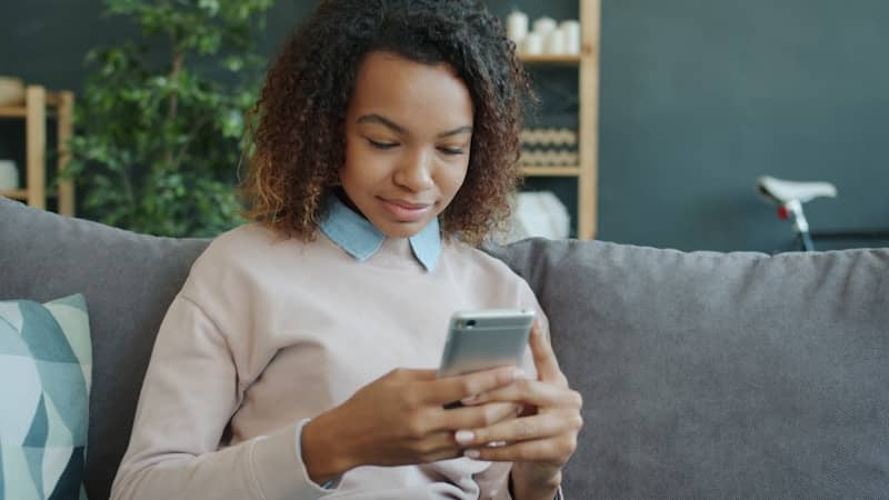 Young woman using a smartphone while sitting on a couch.